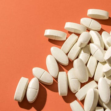 white oval pills scattered on a bright orange surface, highlighting health, medicine, and wellness concepts