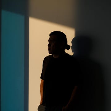 A person standing in shadow beside a wall with light and color contrast.