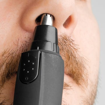 close up man removing hair from nose using electric trimmer on the grey background morning routine