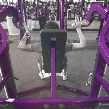 Gym scene featuring an individual exercising on a machine with purple-colored equipment. Gym scene featuring an individual exercising on a machine with purple-colored equipment.
