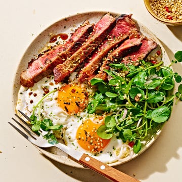 Plate of steak, eggs, and greens alongside a chef wearing an apron.