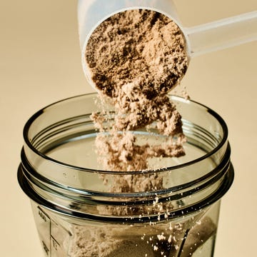 Scoop pouring protein powder into a blender.