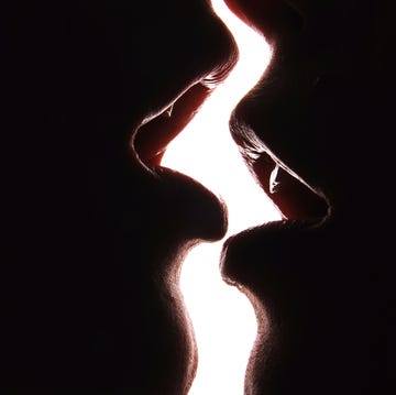 two girls kissing in front of a white wall.
