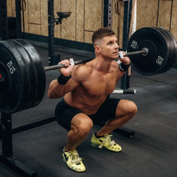 sitting, ready for squats. athletic man performing weightlifting exercises with a barbell in a gym