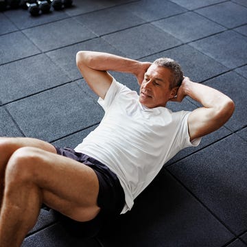 focused senior man in sportswear doing sit ups alone while working out on the floor of a gym