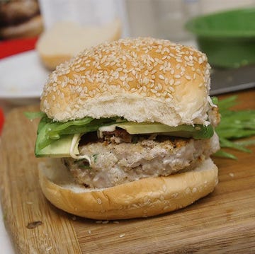 sesame seed burger with greens and toppings on a cutting board