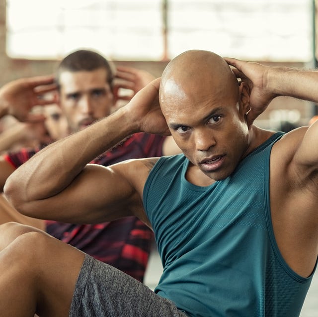 muscular african american man doing sit ups at gym with other people in background mature black man doing abs workout with class at cross training gym muscular guy doing crunches