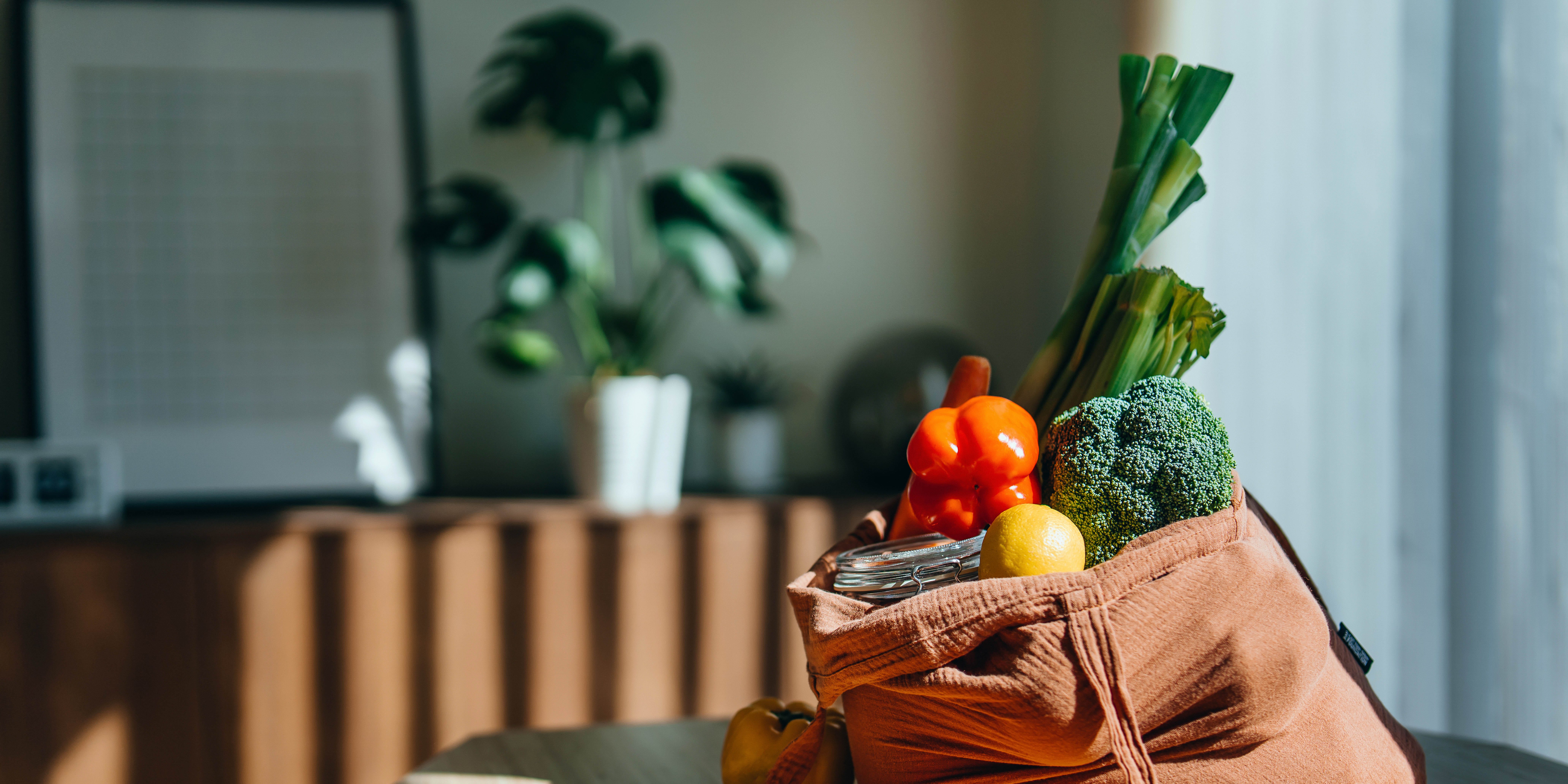eco friendly reusable shopping bag with multi coloured fresh vegetables and groceries on the table at home. shopping with reusable grocery bag