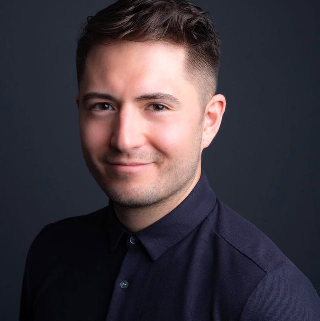 male figure wearing a dark collared shirt against a dark background