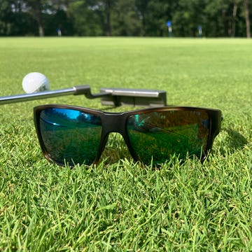 two pairs of sunglasses, a putter, and a golf ball on a putting green