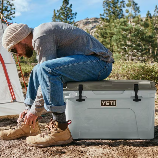Person sitting on a cooler while tying shoelaces outdoors Person sitting on a cooler while tying shoelaces outdoors