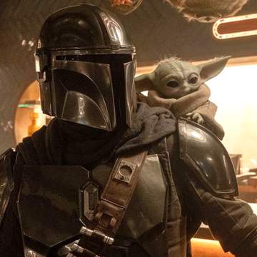 The Mandalorian holding Grogu in a protective stance.