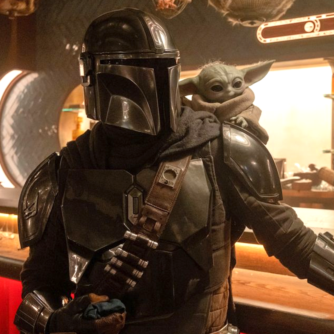 The Mandalorian holding Grogu in a protective stance. The Mandalorian holding Grogu in a protective stance.