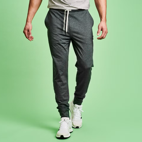 Male model wearing gray joggers and white sneakers against a green background.