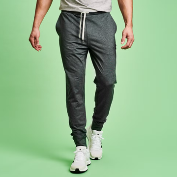 Male model wearing gray joggers and white sneakers against a green background. Male model wearing gray joggers and white sneakers against a green background.